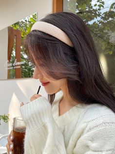 a woman with long hair is holding a drink and looking at her cell phone while wearing a headband