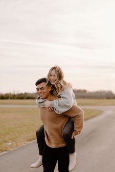 a man carrying a woman on his back in the middle of an empty road with grass