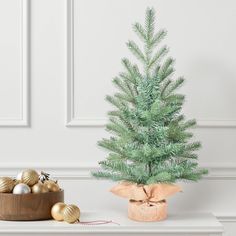 a small green christmas tree sitting on top of a white table next to gold ornaments