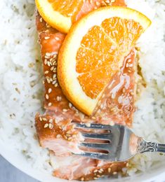 orange slices and sesame seeds on top of rice in a bowl with a fork to the side