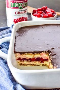 a cake in a white dish with chocolate frosting and cherries on the side