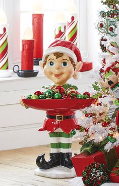 an elf holding a tray with candy canes on it in front of a christmas tree