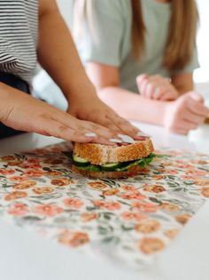 two women are preparing a sandwich on a table