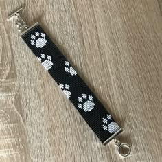 a black and white beaded keychain with paw prints on it, sitting on a wooden surface