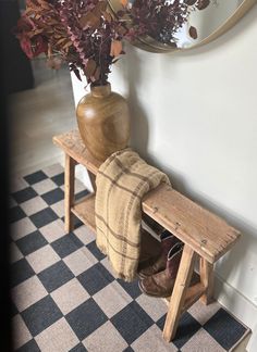 a wooden bench sitting in front of a mirror next to a vase filled with flowers