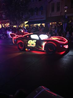 a car with numbers on it driving down the street at night in front of people