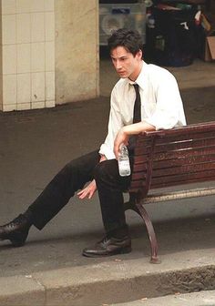 a man sitting on top of a wooden bench next to a sidewalk with a water bottle in his hand