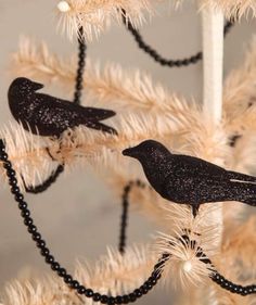 two black birds sitting on top of a white christmas tree with bead garland around it