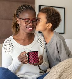 a woman kissing her daughter on the cheek while sitting in front of a couch with a red and black checkerboard coffee mug