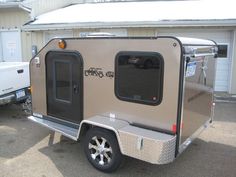 a small trailer is parked in front of a building with two other trailers behind it