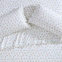 the bedding is made up with white and pink flowers on it's ruffled edges