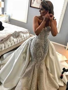 a woman in a wedding dress sitting on the floor next to a bed and looking at her phone