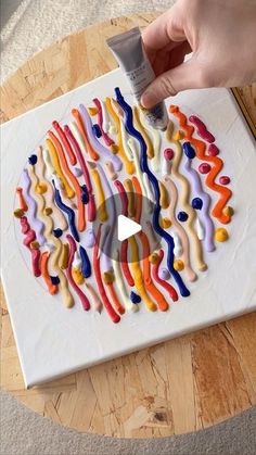 someone is decorating a cake with icing on the top and colorful swirls on the bottom