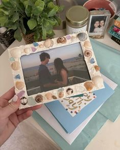 a person holding up a photo frame with seashells and shells on it next to other items