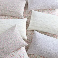 several pillows are arranged in a circle on a floral print bedding set with pink and white flowers