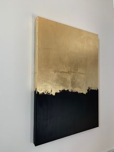 a black and gold painting hanging on the side of a wall in a white room