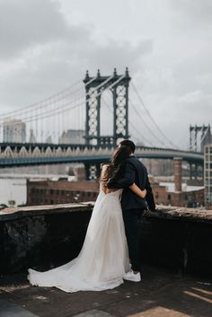 a bride and groom standing on the roof of a building in front of a bridge