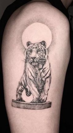 a black and white tiger tattoo on the left upper arm, with a full moon in the background