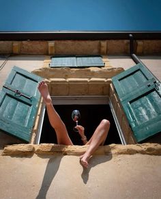 a woman sitting on the ledge of a building holding a wine glass in her hand