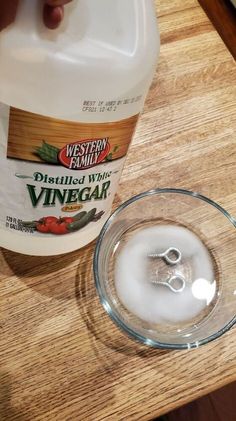 a bottle of vinegar sitting next to a glass bowl on top of a wooden table