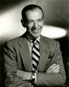 black and white photograph of a man in suit smiling with his arms crossed on his chest