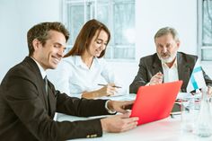 three business people sitting at a table and one is holding a red piece of paper