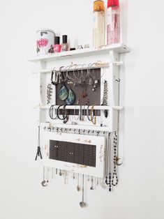 a white wall mounted jewelry rack with lots of necklaces and earrings hanging on it