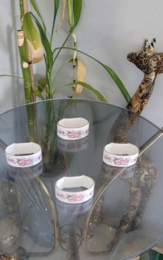 a glass table with five cups on it and a giraffe figurine in the background