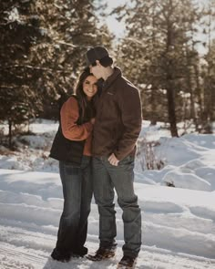 a man and woman standing in the snow with their arms around each other, smiling