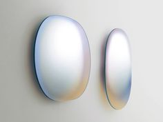 two oval shaped mirrors mounted to the side of a white wall next to each other