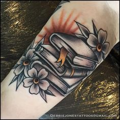 a tattoo with an old book and flowers on it