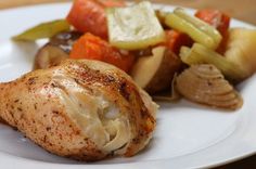 a white plate topped with chicken, vegetables and potatoes on top of a wooden table