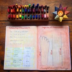 an open book with colored crayons next to it on top of a wooden table