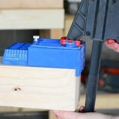 a person holding a piece of wood with some tools on it and another hand holding a tool