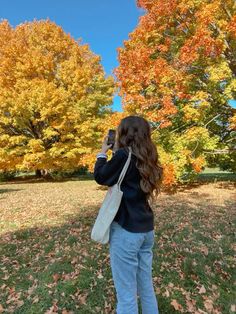 a woman taking a photo with her cell phone in front of some trees and leaves