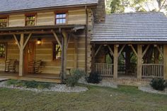 a log cabin with porches and covered in wood shingles, surrounded by trees