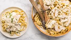 two plates of pasta with chicken and parmesan cheese on the side next to a wooden spoon