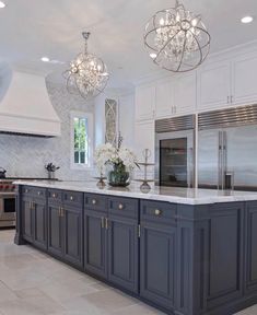 a large kitchen with marble counter tops and gray cabinets, chandeliers above the island