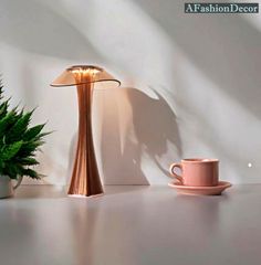 a table lamp sitting next to a pink cup and saucer on a white surface