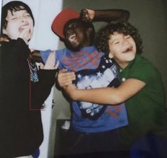 three young boys are posing for a photo with one boy wearing a red hat and the other is laughing