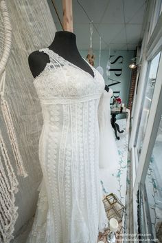 a white dress is on display in a store window with other dresses hanging up behind it