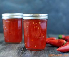 two jars filled with red peppers sitting on top of a wooden table