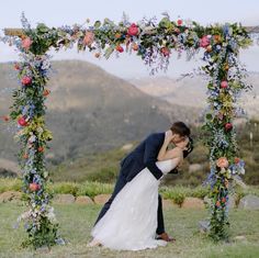 a bride and groom kissing under an outdoor wedding ceremony arch with flowers on the side