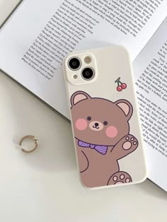 a phone case with a bear on it sitting next to an open book and ring