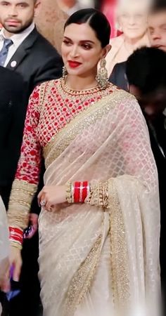 a woman in a white and red sari is walking down the street with other people behind her