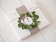 a gift wrapped in white paper and tied up with a green leaf wreath on top