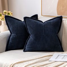 two blue pillows sitting on top of a white couch next to a vase with flowers