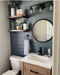 a white toilet sitting under a bathroom mirror next to a wooden sink vanity and shelf