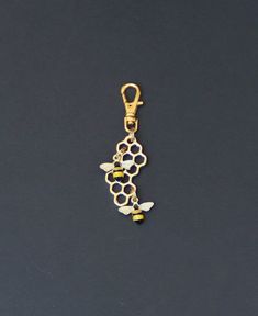 a gold key chain with bee charms hanging from it's side on a black surface