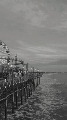 a ferris wheel sitting on the side of a pier next to the ocean in black and white